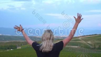 一个女人走在葡萄园的高处，站着，举起双手，快乐地<strong>蹦蹦</strong>跳跳。